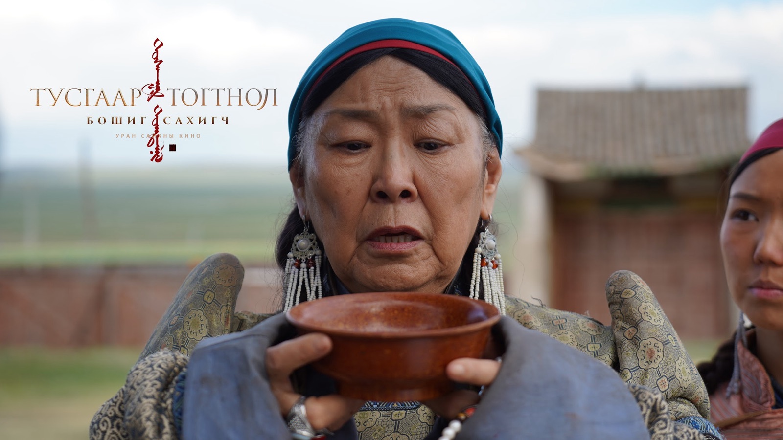 An older woman in a blue headscarf holding a wooden bowl
