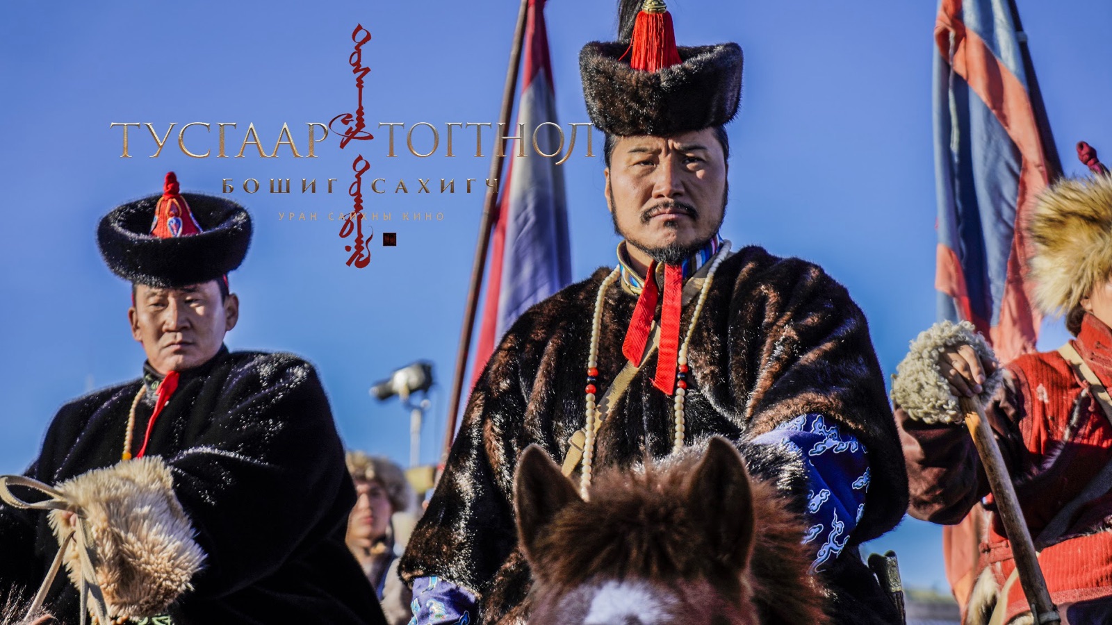 Two riders in fur hats on horseback, flags behind them against a blue sky